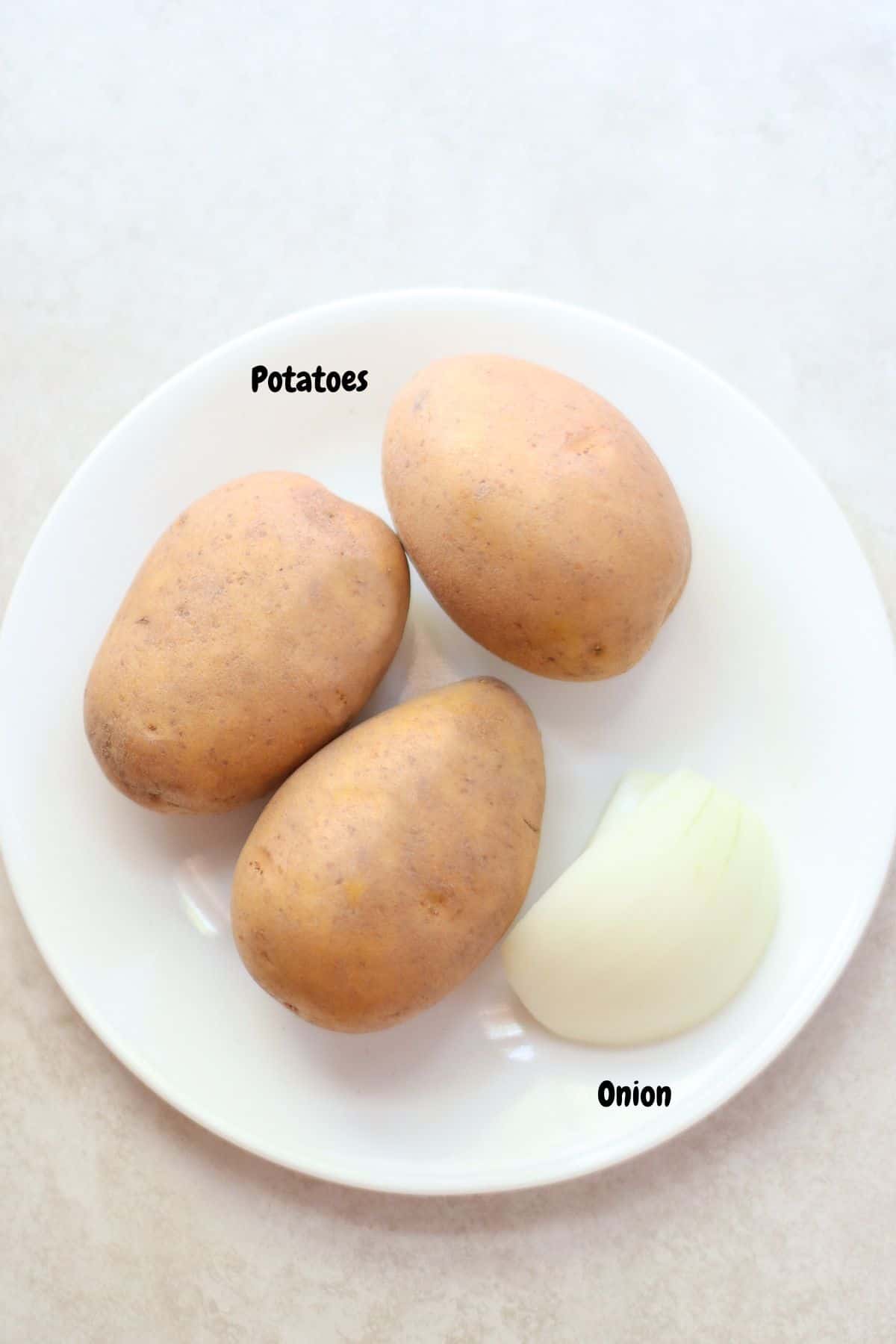 3 potatoes and half of an onion on a plate.