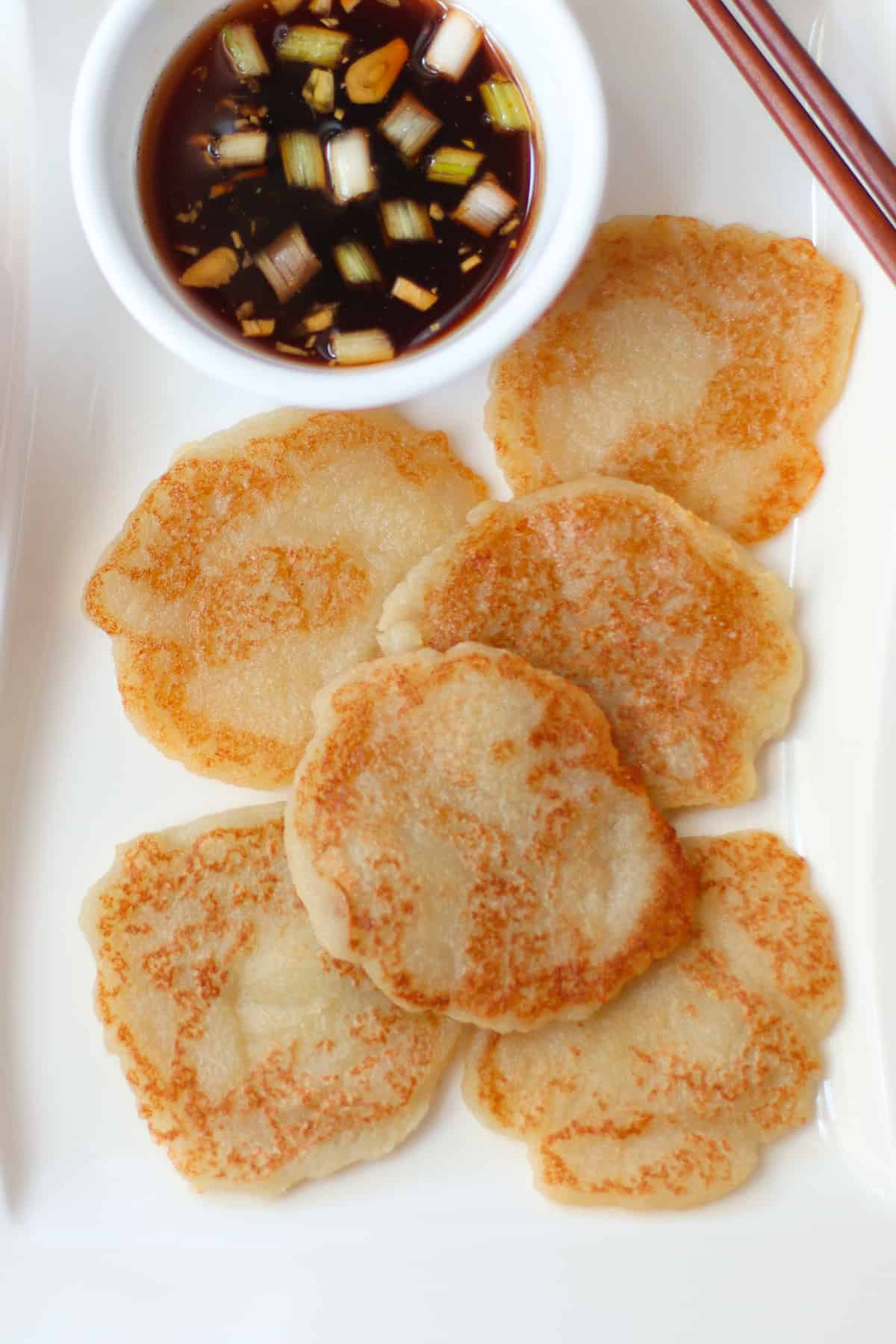 Golden brown gamjajeon with dipping sauce on a white plate.