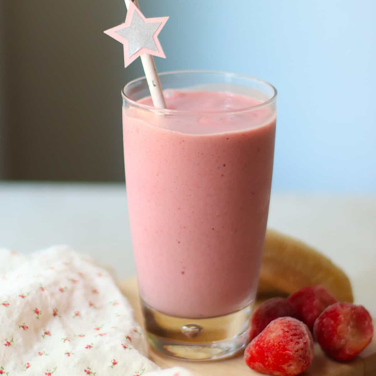 Strawberry banana milkshake in a glass with a straw and strawberries in the background.