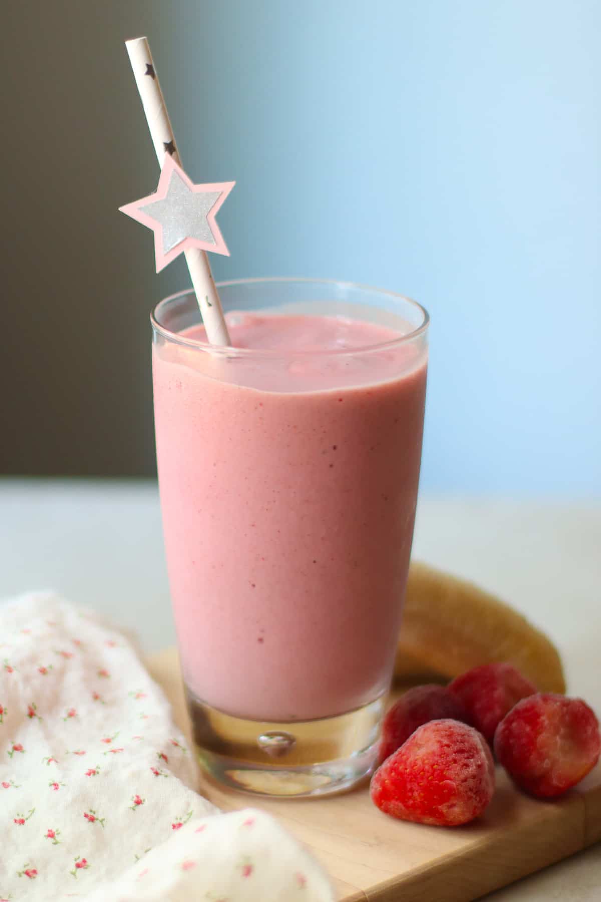 Strawberry banana milkshake in a glass with a straw and strawberries in the background.