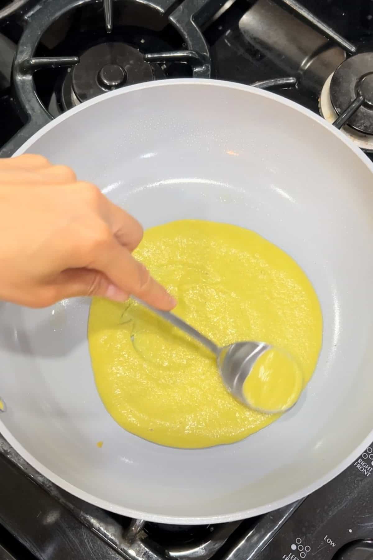 Spreading the lentil wrap batter onto a skillet evenly with a back of a spoon.