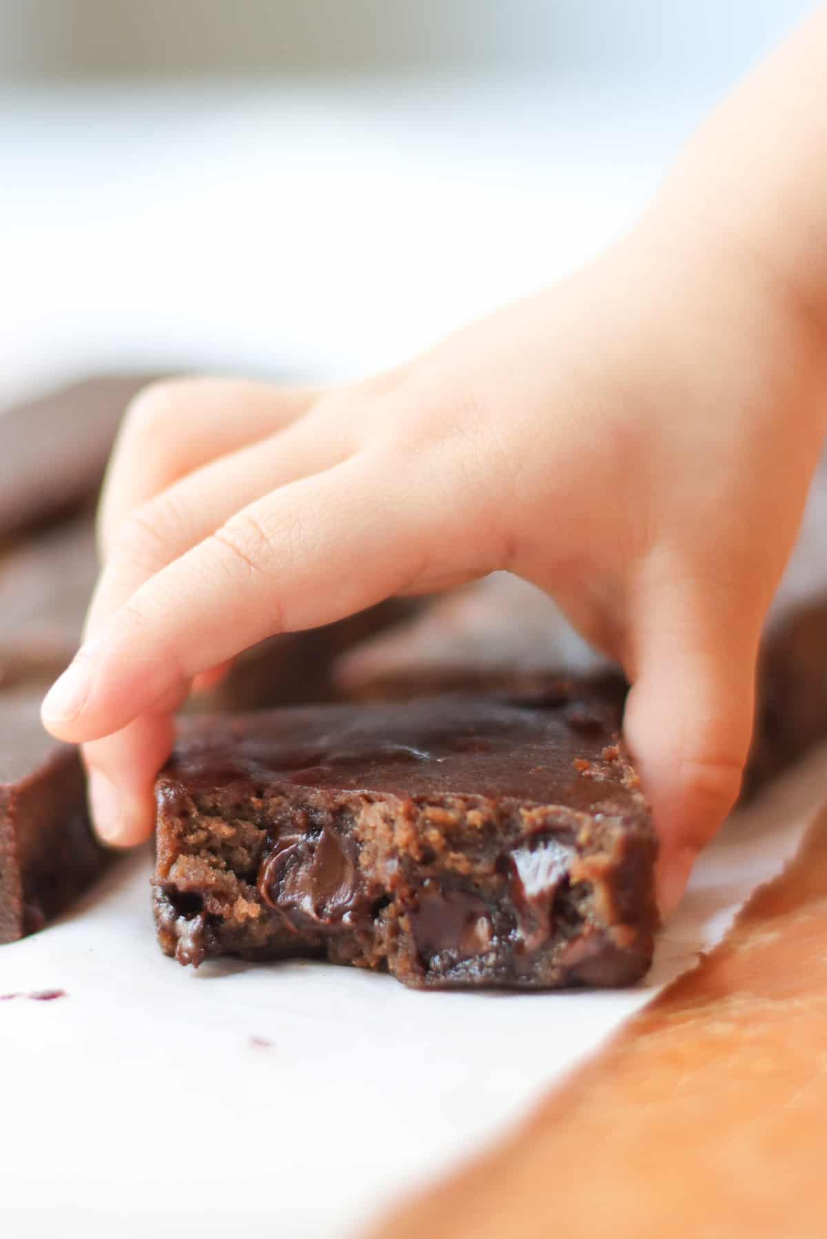 A close up shot of a brownie with a bite taken and toddler holding it.