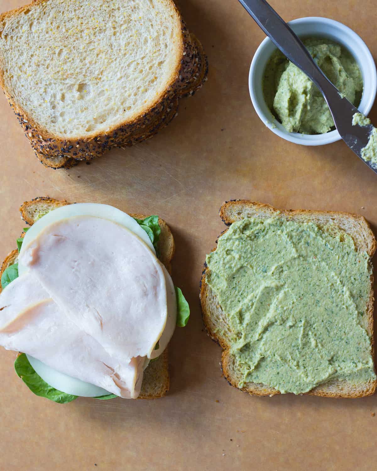 sandwich slice with pesto spread and another slice with lettuce, cheese, and turkey.