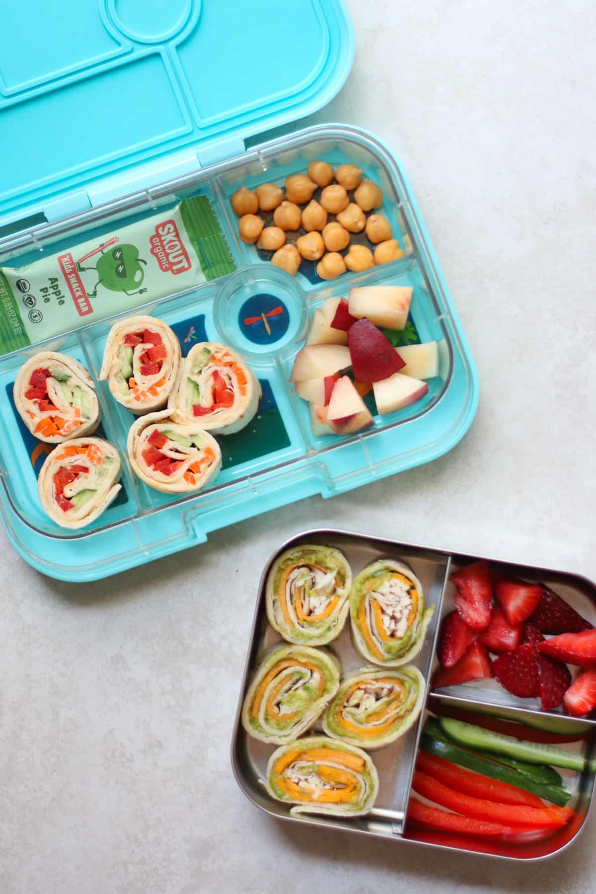 Two lunchboxes each with pinwheel sandwiches, fruits, and vegetables.