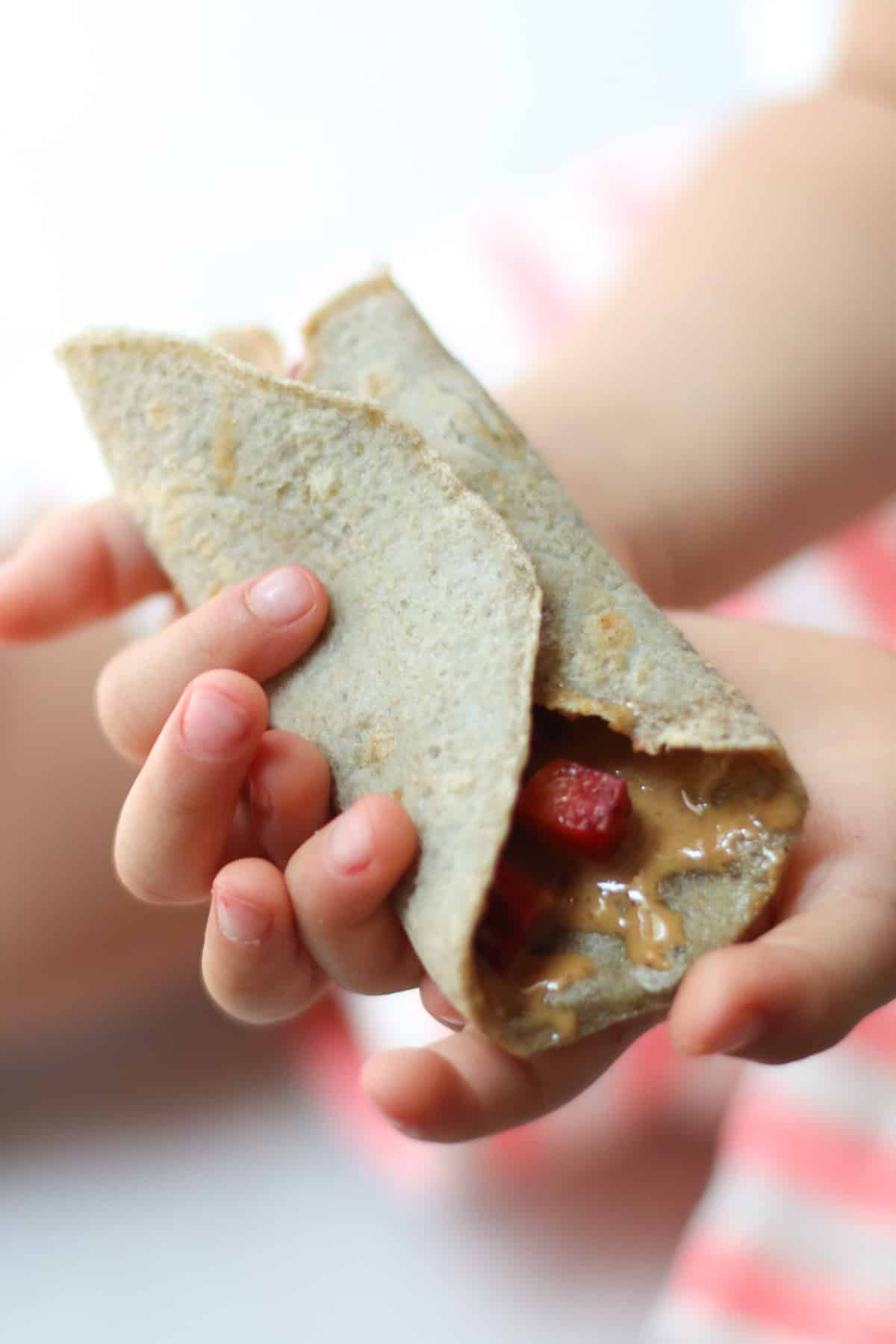 Toddler's hands holding quinoa wrap filled with strawberries and peanut butter.