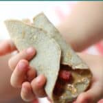 Toddler's hands holding quinoa wrap filled with strawberries and peanut butter.