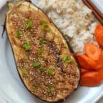 An overhead shot of cooked eggplant with green onions, rice, and carrots.