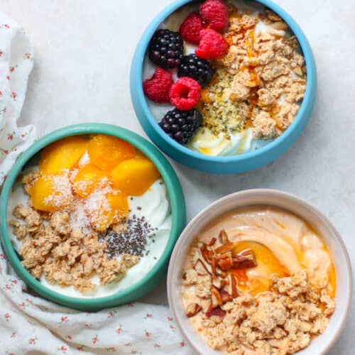 Three yogurt bowls with granola and various toppings.