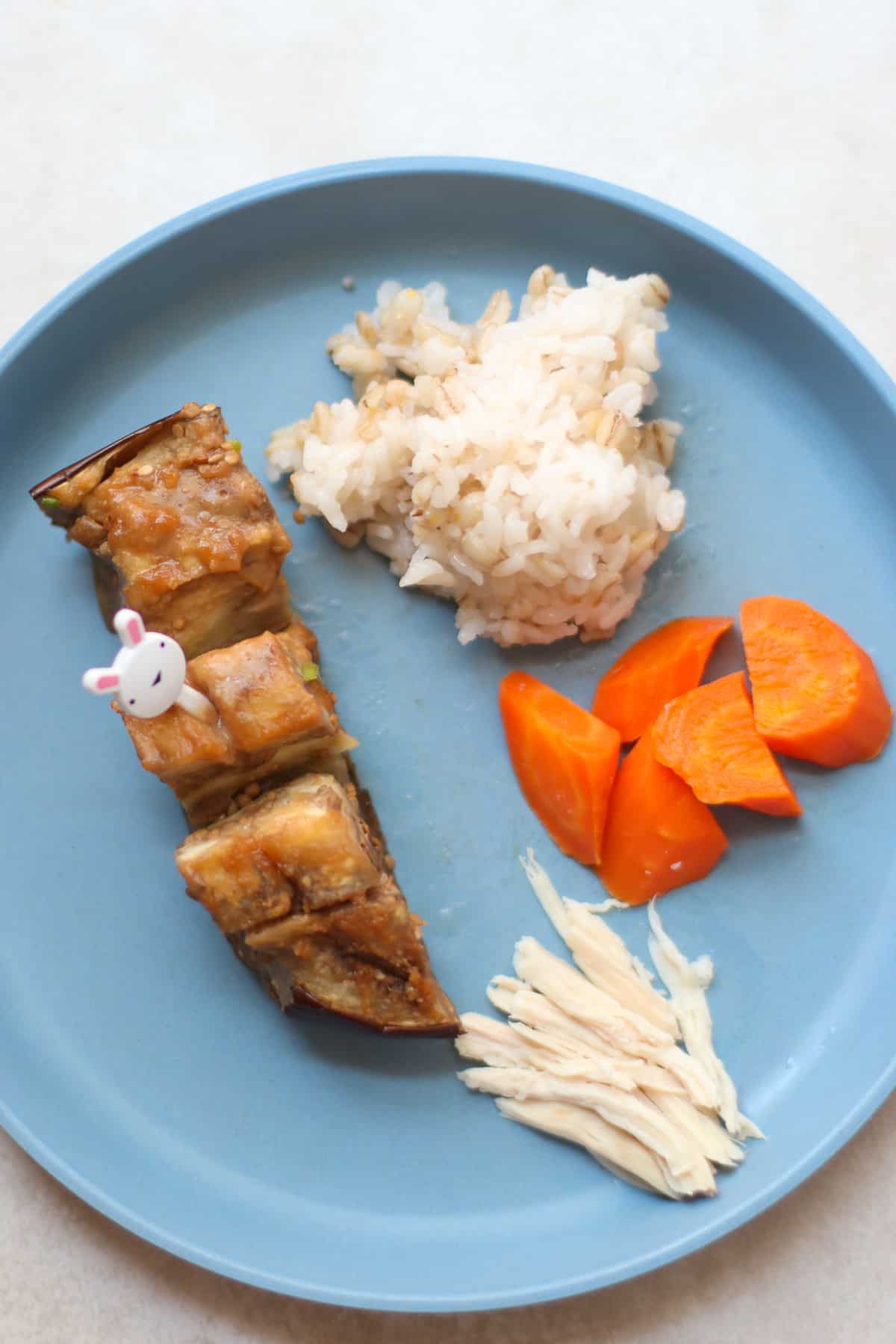 A toddler's plate with a strip of miso aubergine, rice, carrots, and chicken.