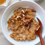 A close up shot of cooked pumpkin oatmeal with milk and pecans.