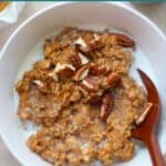 A close up shot of cooked pumpkin oatmeal with milk and pecans.