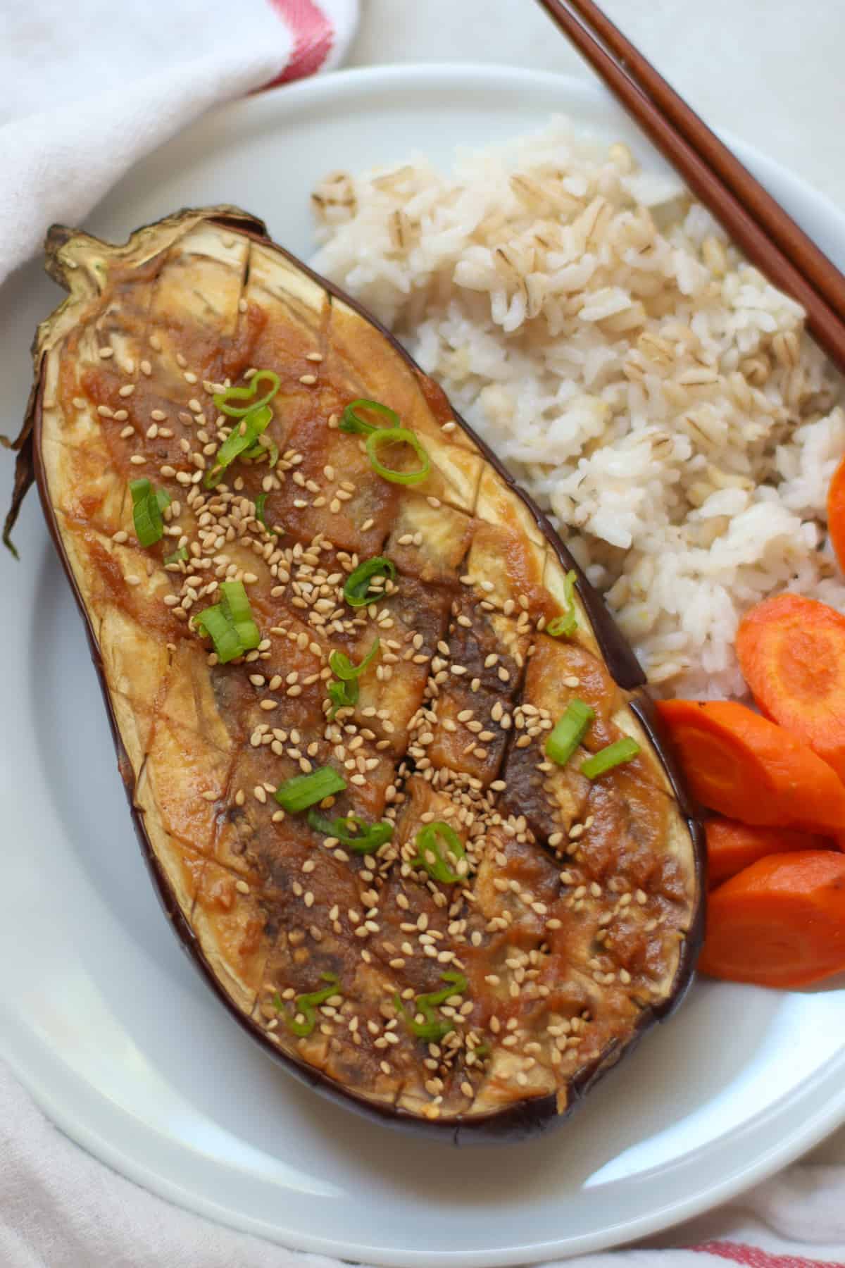 An overhead shot of cooked eggplant with green onions, rice, and carrots.