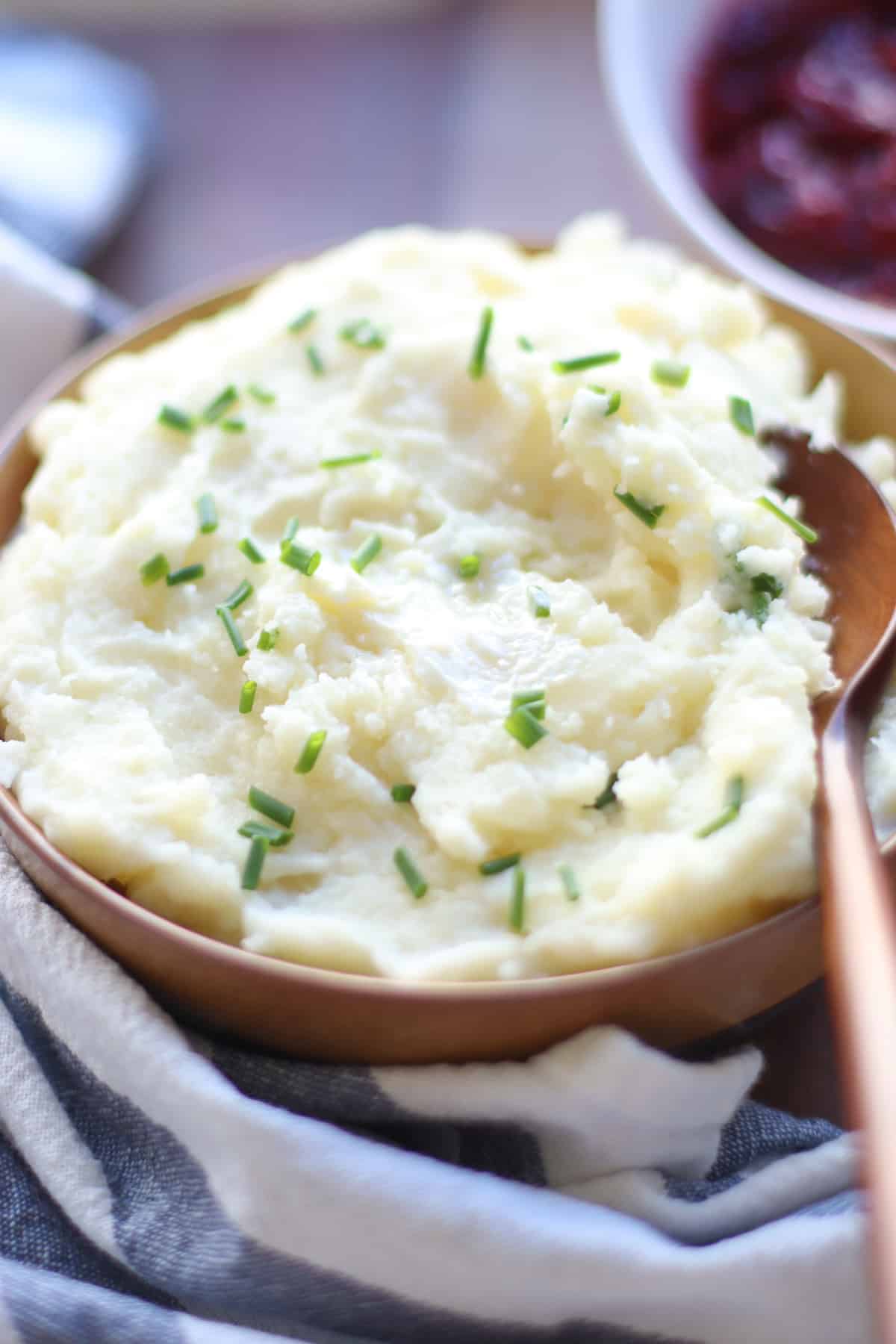 Creamy cheesy mashed potatoes in a large bowl with fresh chives.