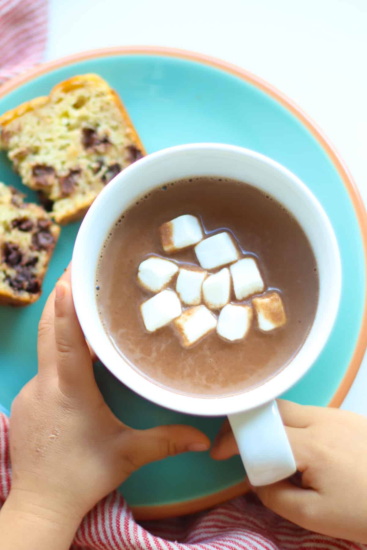 An overhead shot of hot chocolate with marshmallows with toddler's hand.