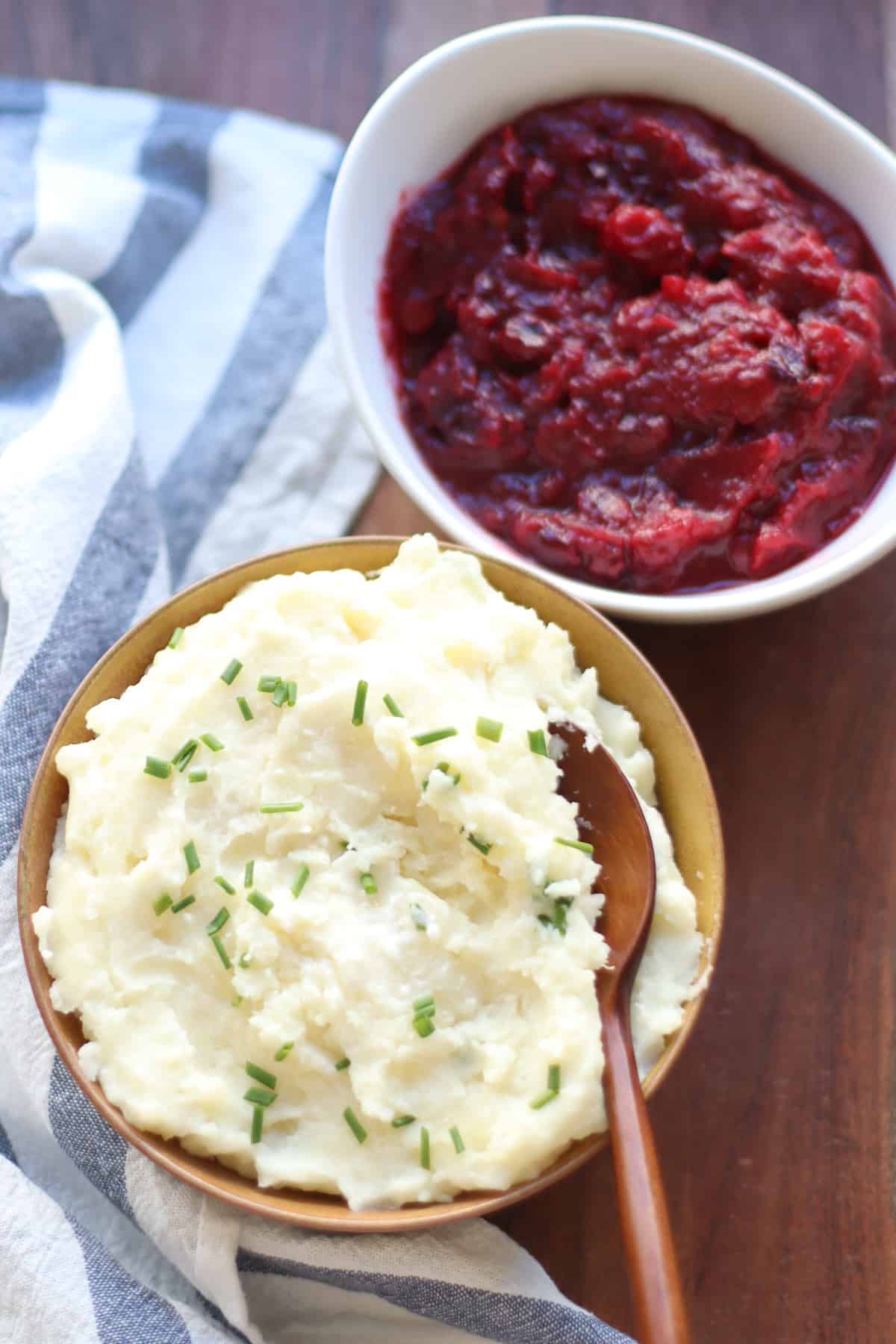 Mashed potatoes in a large bowl and a bowl of cranberry sauce behind it.