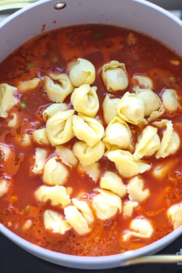 Tortellini being added to simmering sauce.