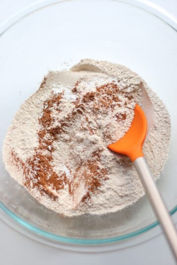 Dry ingredients combined in a glass bowl with an orange spoon.