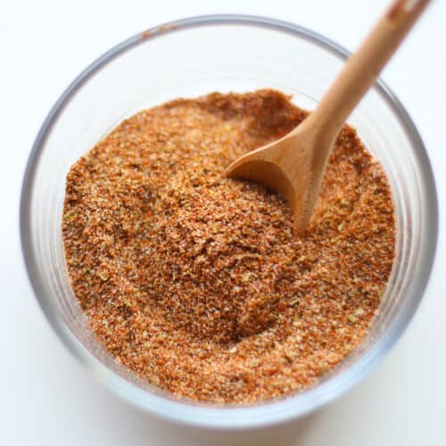 Taco seasoning blend combined in a glass bowl with a wooden spoon.