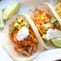 Chicken tacos in a white plate with lime wedges.