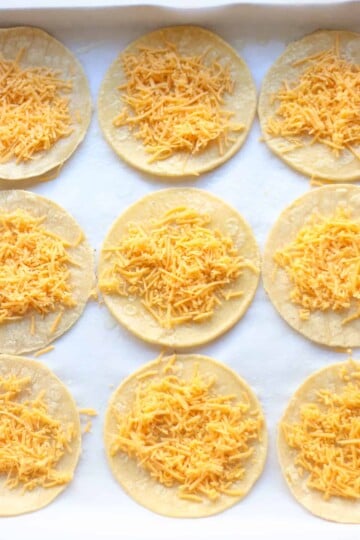 Tortillas laid on baking sheet spread with cheese.