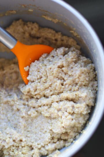Cooked quinoa porridge in a pot with orange spatula.