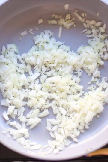 Chopped onions sautéing in a blue skillet.