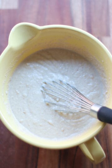Ingredients of sheet pan pancakes combined in a cream bowl with a whisk.