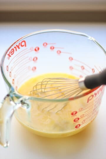 Eggs that have been beaten with a whisk in a clear container.