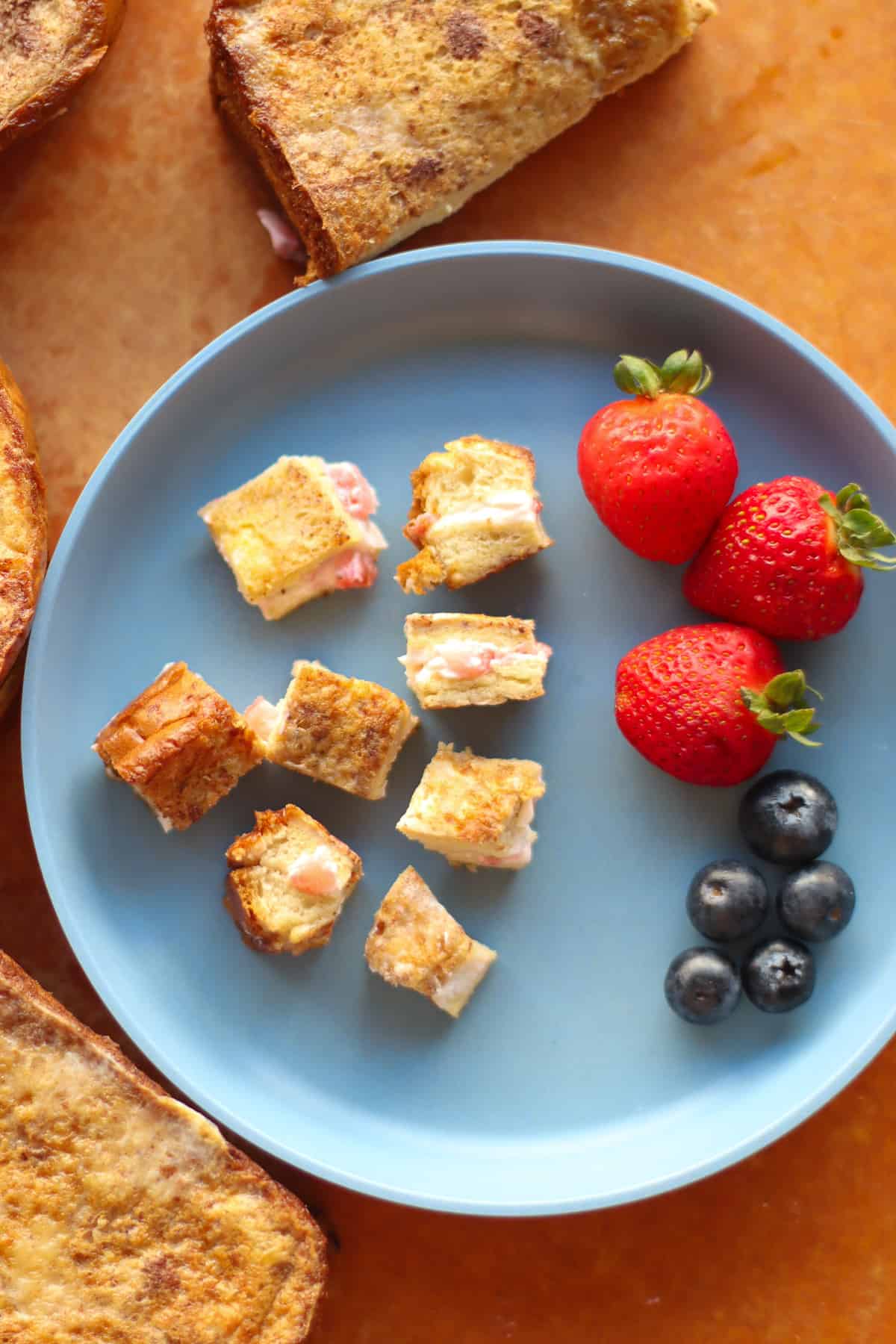 Stuffed French toast cut into bite-sized pieces with strawberries and blueberries on the side.