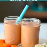 Two mason jars, one with a blue straw, filled with the smoothie on a wooden cutting board with sliced carrots and sliced banana.