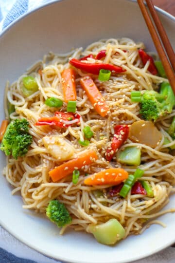 Vegetable stir fry noodles with sesame seeds in a white bowl.