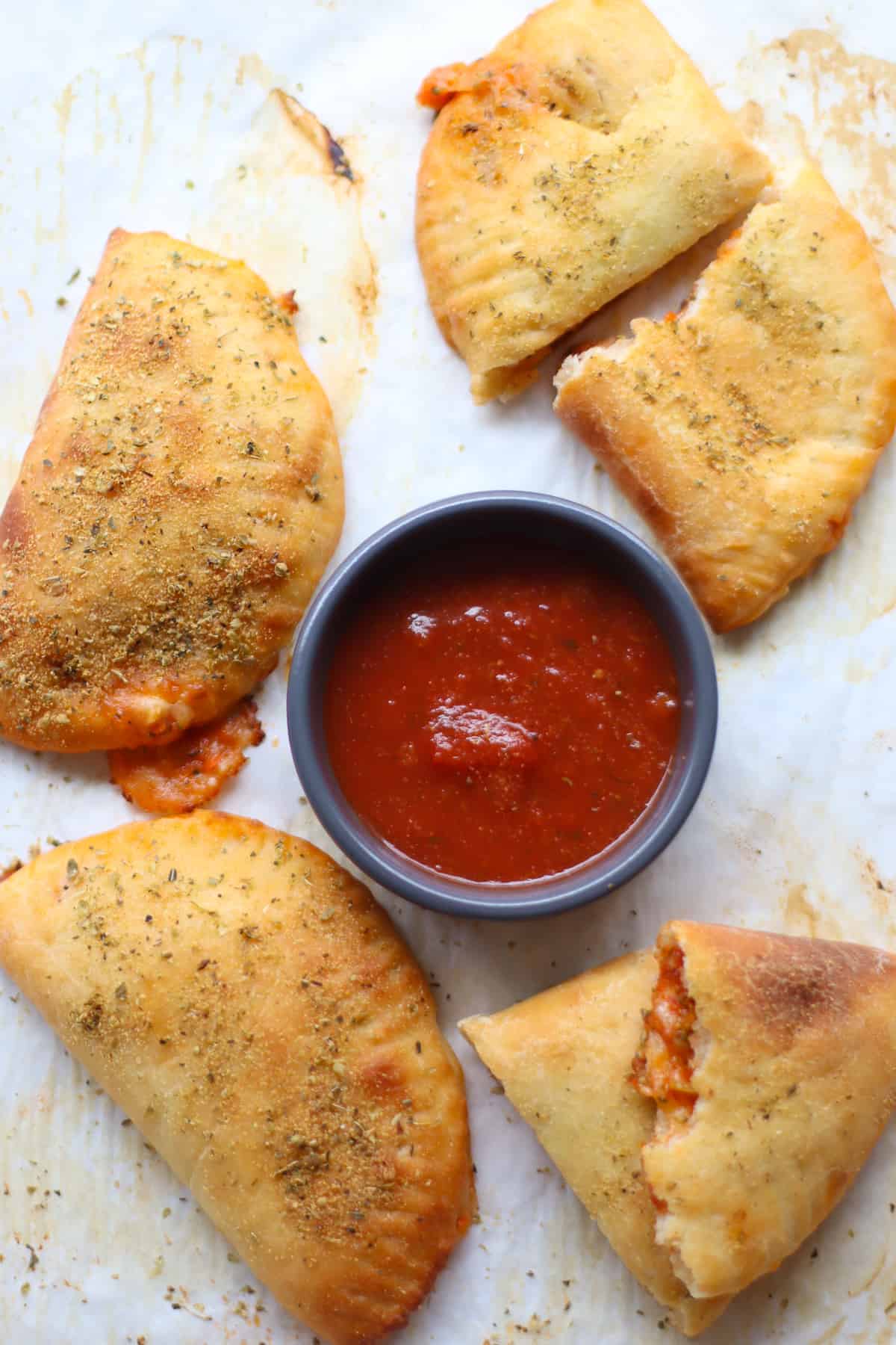 Cooked pizza pockets arranged around a dipping container of pizza sauce.