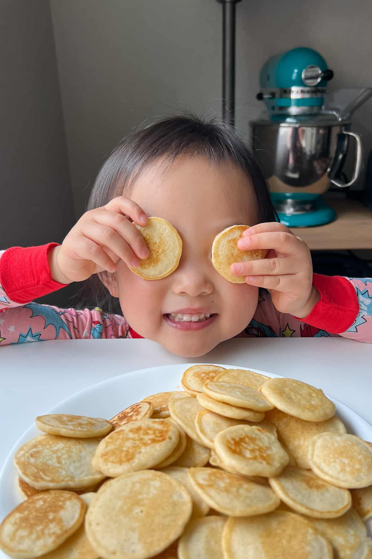 Toddler holding two pancakes up to her eyes.