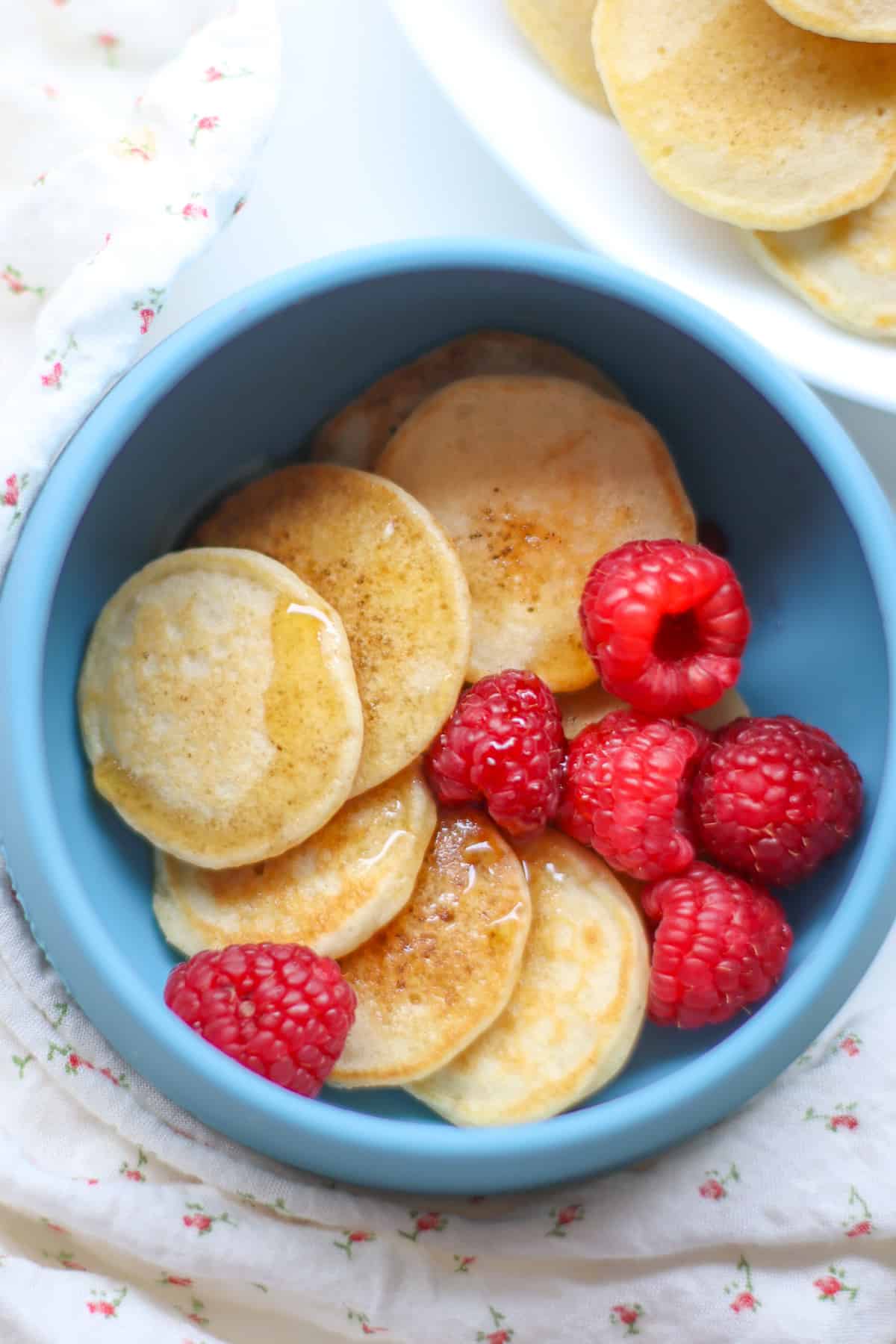 Six pancakes and raspberries in a blue bowl.