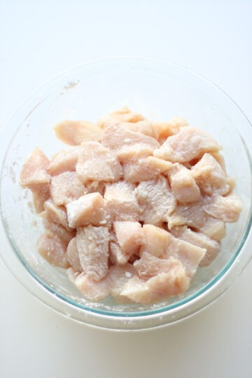 Diced chicken tossed with corn starch in a clear glass bowl.