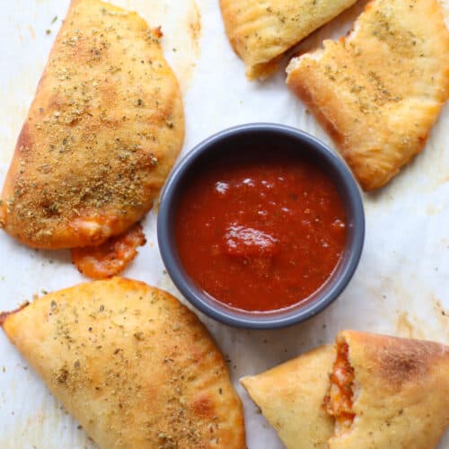 Cooked pizza pockets arranged around a dipping container of pizza sauce.