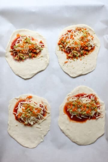 Four flat pieces of dough with pizza sauce and toppings on half of them.