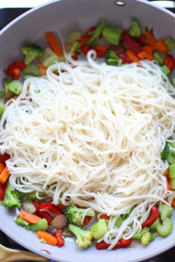 Vegetables underneath noodles in a skillet.