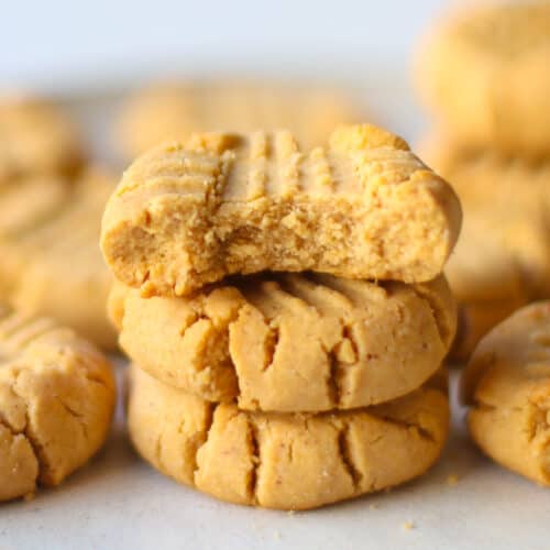 A stack of three baked peanut butter cookies, the top one with a bite taken out of it.