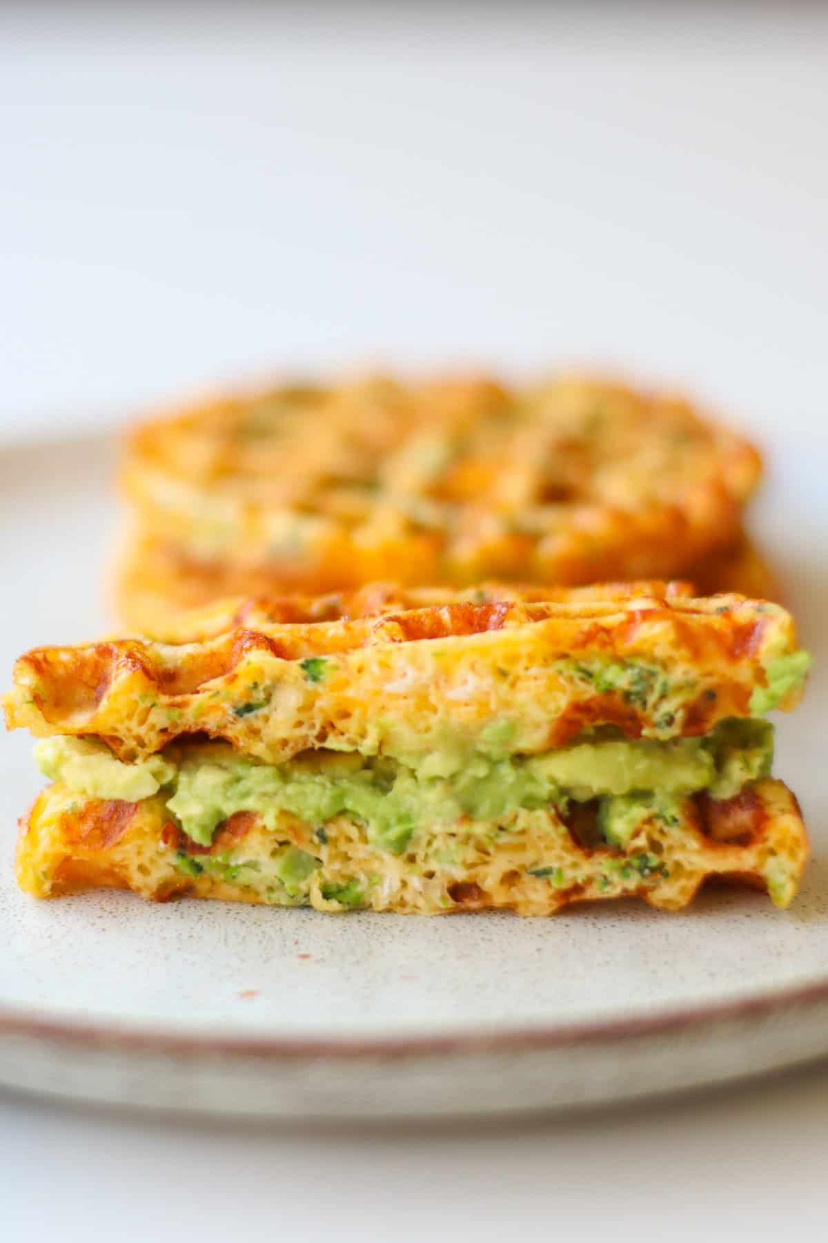 Waffle sandwich with avocado as filling. In the background are two more waffles.