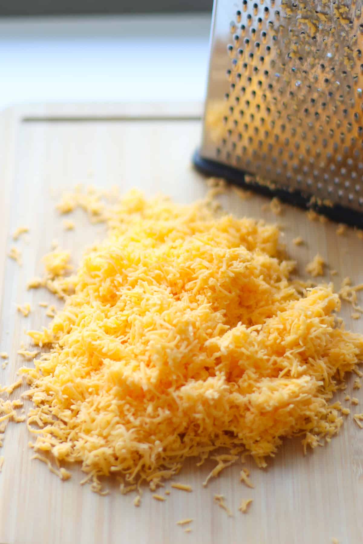 A pile of finely shredded cheese in front of a cheese grater.