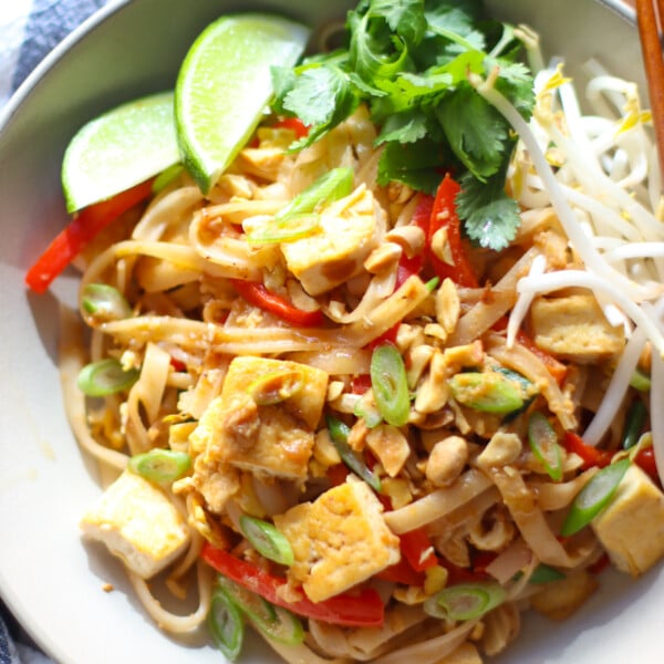 Finished Tofu Pad Thai dish garnished with 2 lime wedges, cilantro, bean sprouts, sliced scallions and peanuts.