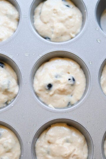 Blueberry muffin batter divided into cups in a muffin tin.