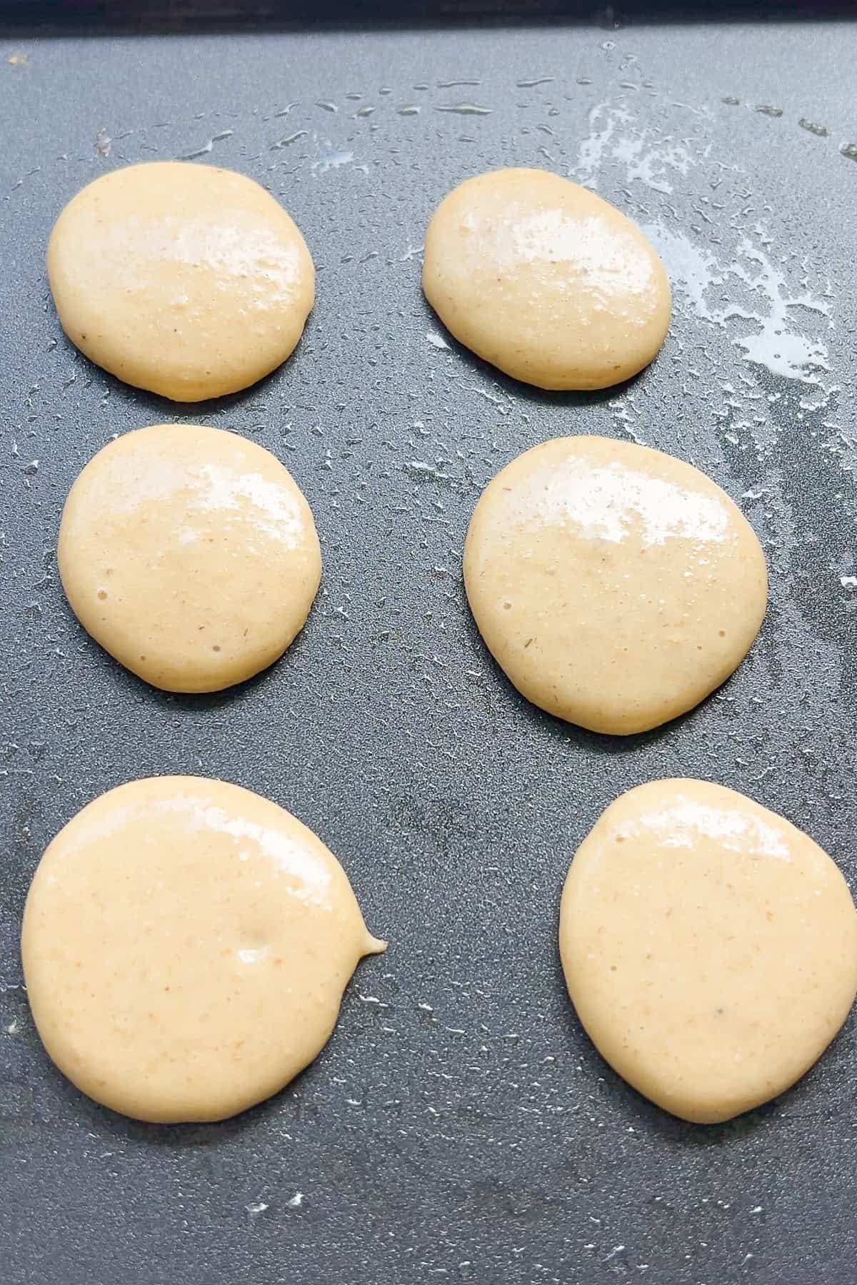 Pancake batter poured on a griddle for 6 pancakes.