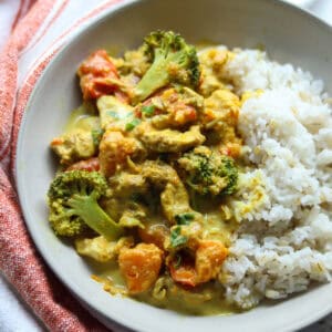 A serving of slow cooker chicken curry in a bowl alongside a serving of white rice.