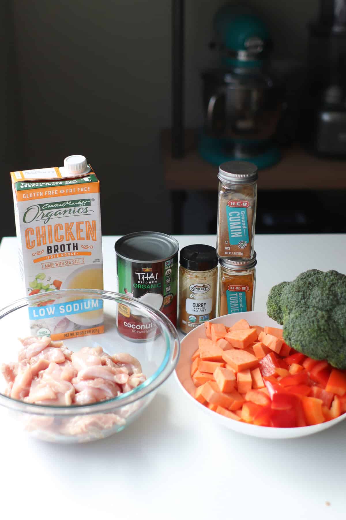 All ingredients for this slow cooker chicken curry sitting on a white countertop, with the chicken, sweet potatoes, and peppers cut up in prep bowls.