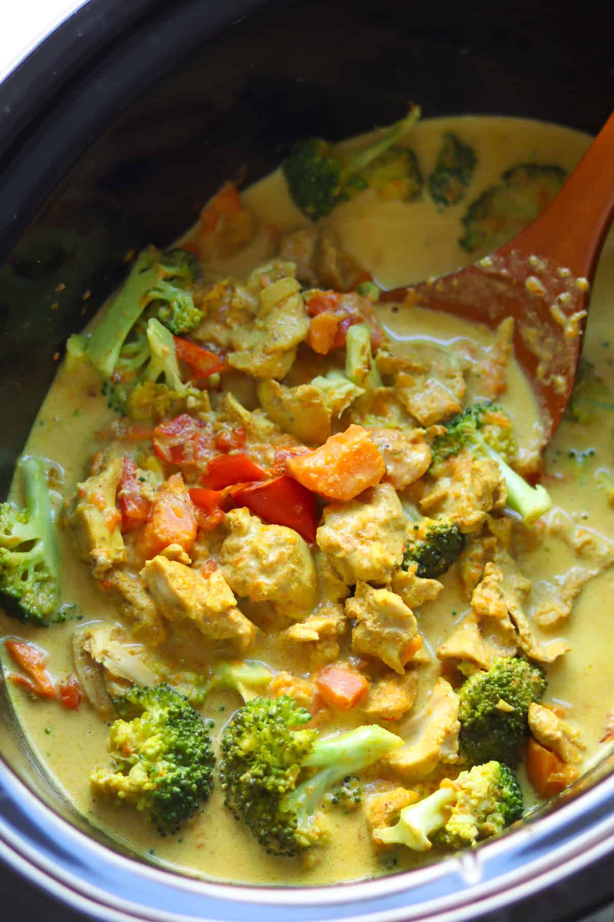 Finished chicken curry in the black crock with a wooden spoon inserted in the mixture.