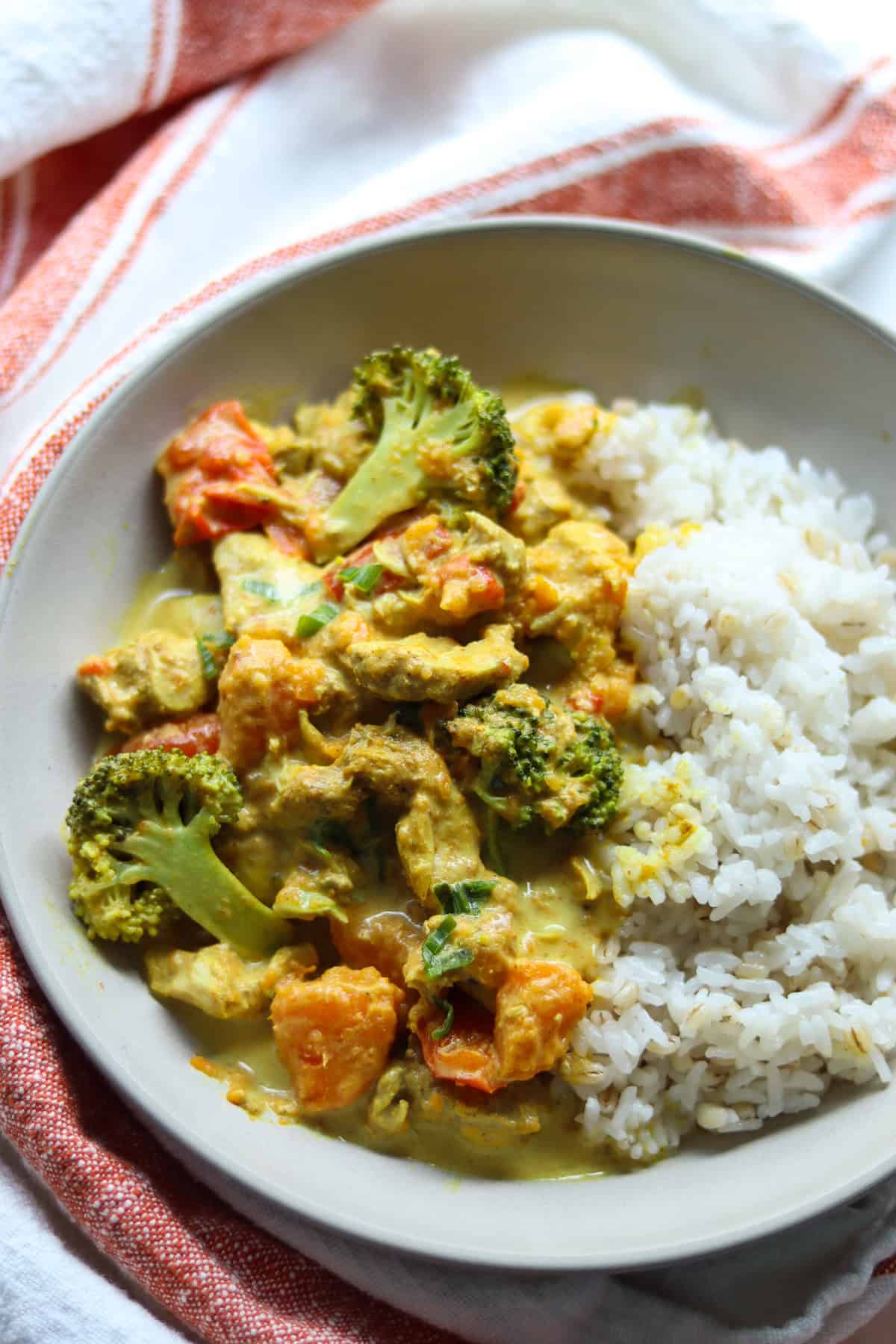 A serving of slow cooker chicken curry in a bowl alongside a serving of white rice.