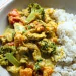 A serving of slow cooker chicken curry in a bowl alongside a serving of white rice.