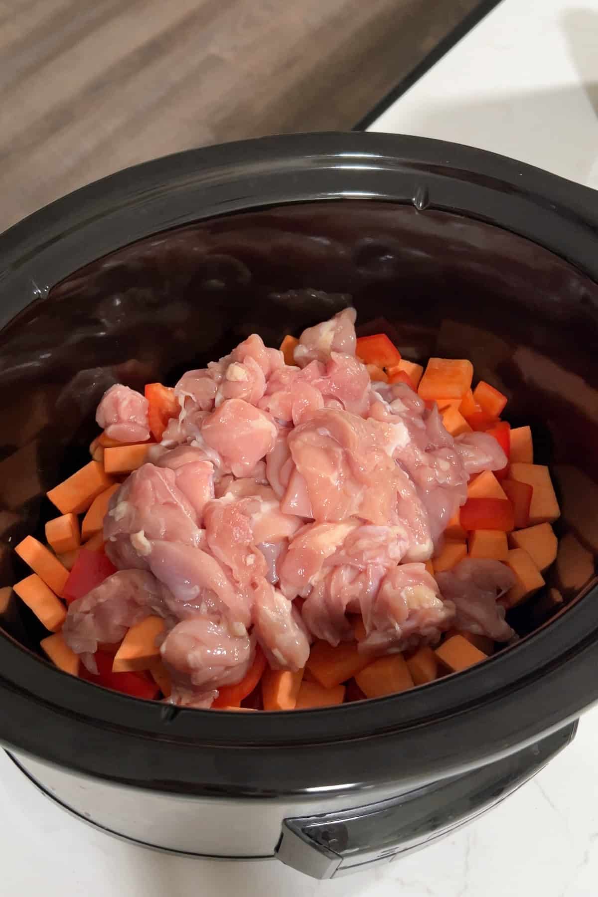 Diced sweet potato, sliced bell pepper, and cubed chicken thighs in the slow cooker.